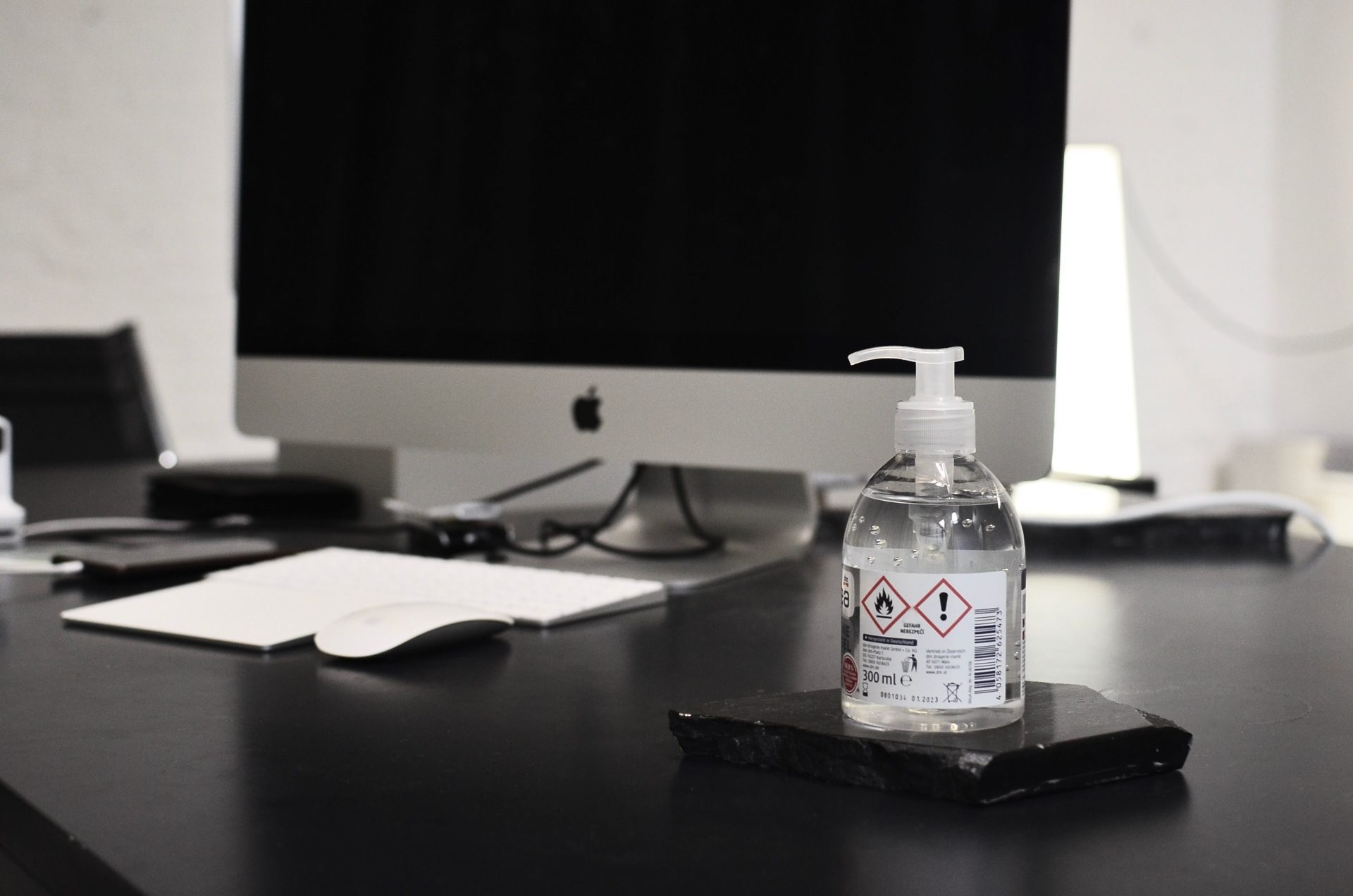 Bottle of antibacterial gel for hands placed on table against modern monitor with black screen in contemporary workspace