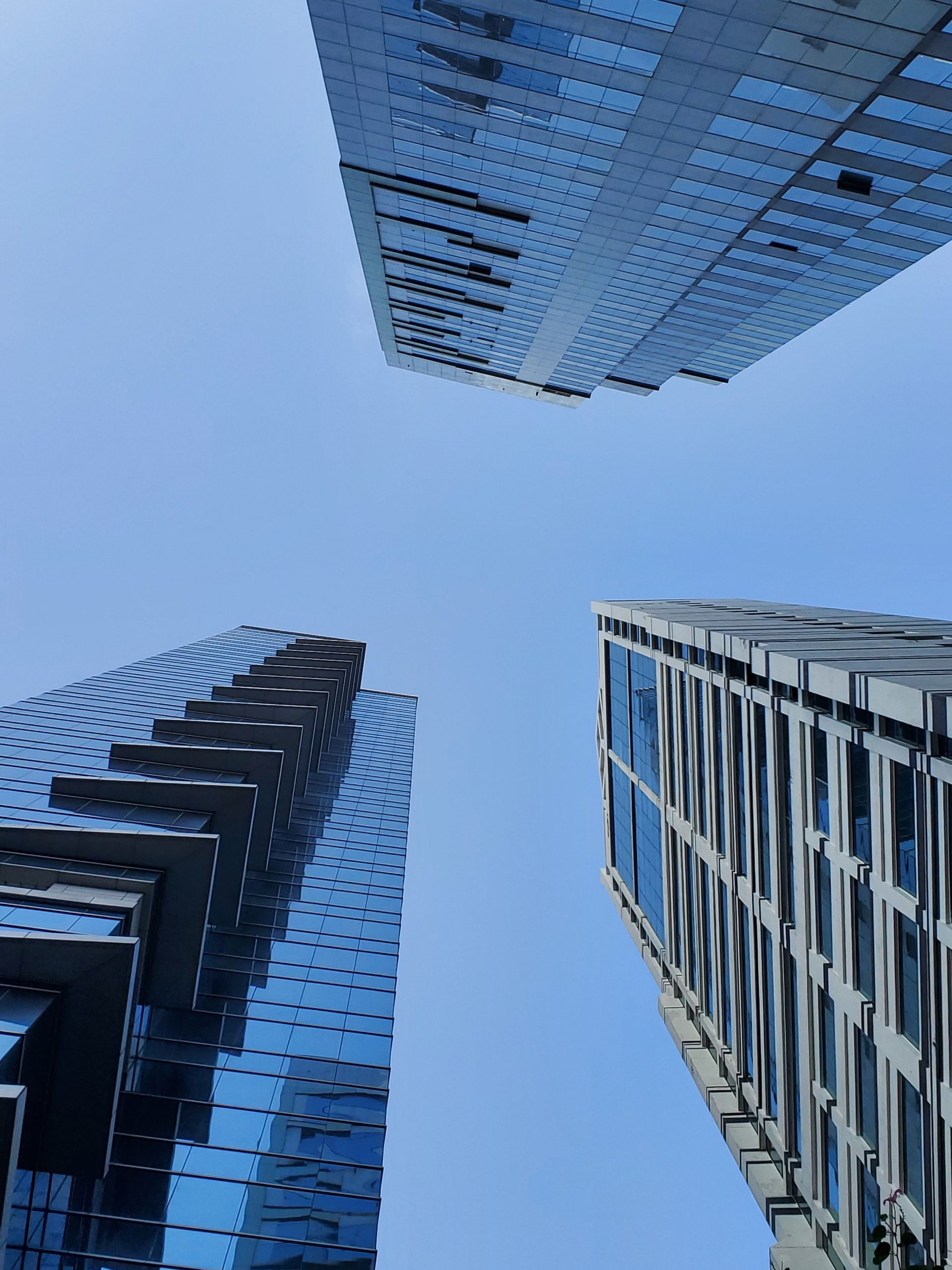 Low-angle shot of glass skyscrapers reaching towards a clear blue sky.